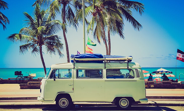 Mobil VW Combi yang terparkir di pinggir pantai sangat cocok menggambarkan liburan impian di musim panas